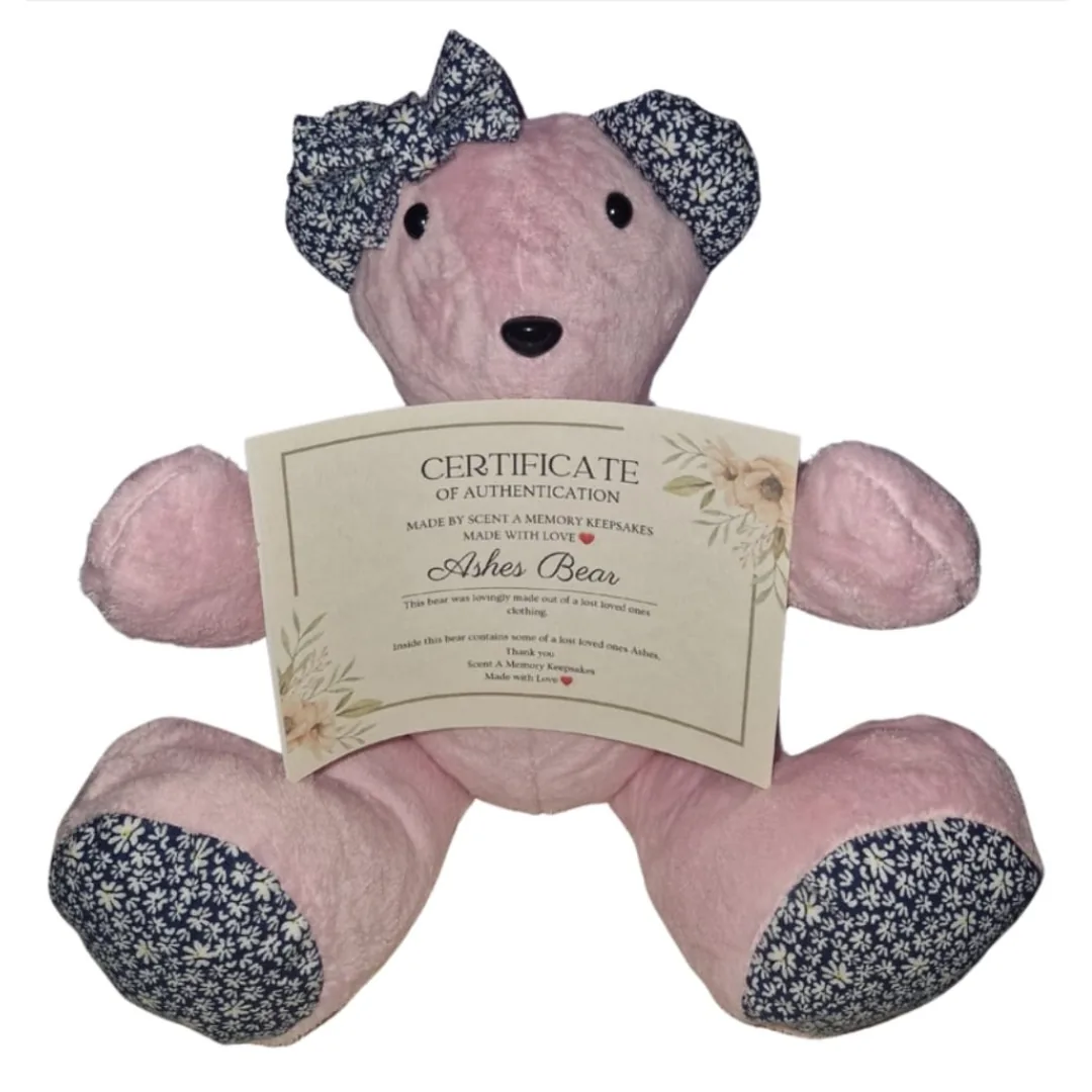 Pink ashes bear with navy floral ears, paw pads and bow, holding a Certificate of Authentication