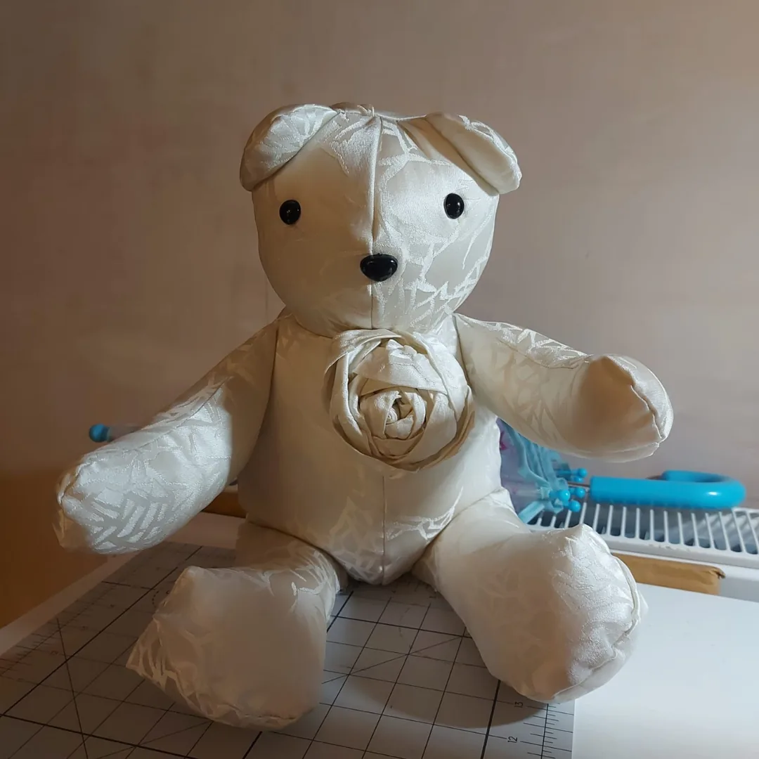 Close view of an ivory wedding dress memory bear with a hand rolled fabric rose on its chest