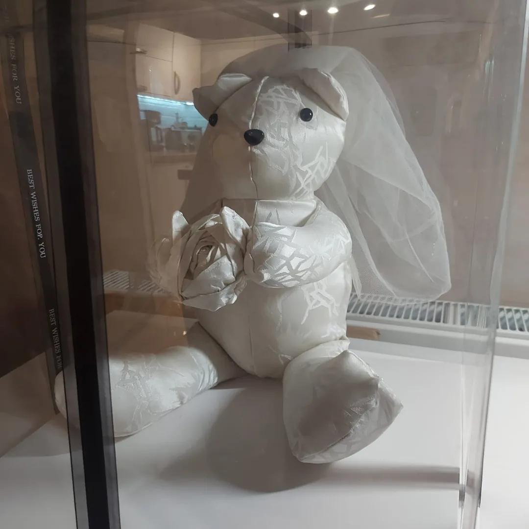 Ivory wedding dress memory bear wearing the veil and holding a fabric rose, sitting in a clear display box